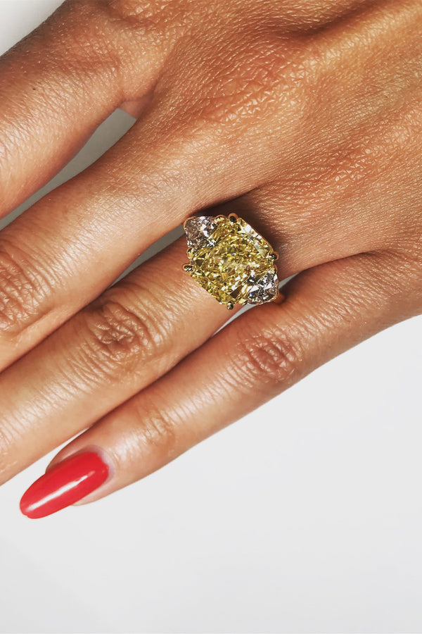 Hand wearing a ring with a large yellow gemstone on a light gray background